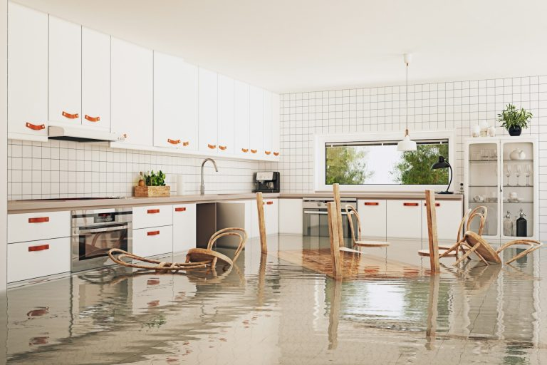Flooded kitchen with water covering the floor, overturned chairs, and modern white cabinetry.